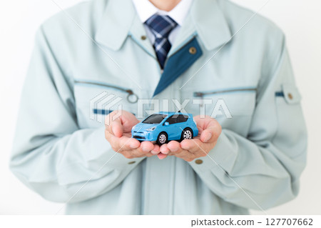 A middle-aged male businessman wearing green work clothes and holding a miniature car 127707662