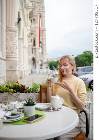 Woman enjoying tea at outdoor cafe near historic European building facade 127708317