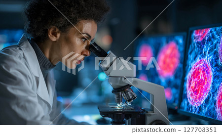 A young female scientist working in a laboratory. She is carefully looking through a microscope. Laboratory, scientific research. 127708351