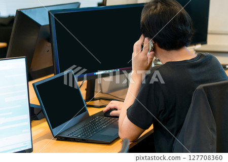 Man talking on the phone while working at a computer screen in an office 127708360