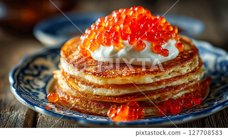 Thin and fluffy pancakes stacked on a ceramic plate. The top pancake is decorated with a spoonful of sour cream, on which the caviar is located. 127708583