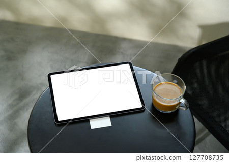 Digital tablet with blank screen on a black round table beside a glass cup of coffee Digital tablet with blank screen on a black round table beside a glass cup of coffee 127708735