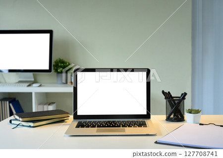 Clean office desk featuring a laptop with a white screen, notebooks, pens, and a potted plant. Clean office desk featuring a laptop with a white screen, notebooks, pens, and a potted plant. 127708741