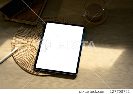Digital tablet with blank screen on wooden desk beside coffee cup in soft morning light Digital tablet with blank screen on wooden desk beside coffee cup in soft morning light 127708761