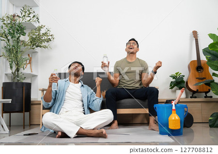 Celebration of Friendship. Two young men joyfully raising water bottles after cleaning their space. 127708812