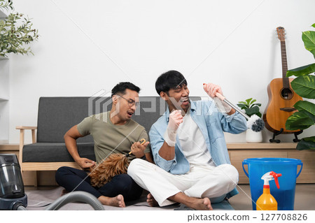 Joyful Cleaning Experience. Two friends creating music while tidying up their living space. 127708826