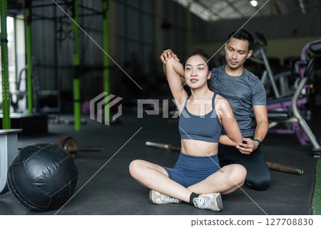 Personal Training and Fitness Coaching. A trainer assisting a woman with stretching exercises in a gym. 127708830