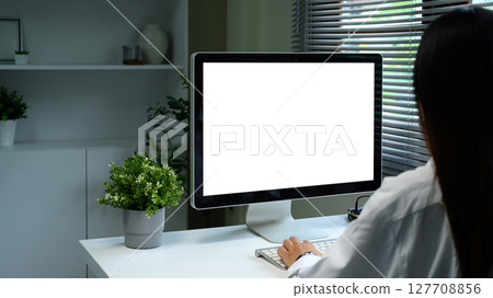 Back view of businesswoman working at desktop computer with blank screen Back view of businesswoman working at desktop computer with blank screen 127708856