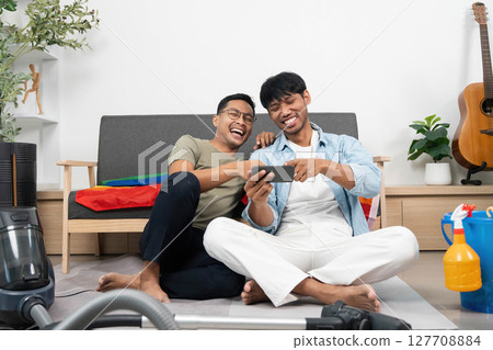 LGBTQIA Friendship and Laughter. Two young men enjoying a fun moment while cleaning their home. LGBTQIA Friendship and Laughter. Two young men enjoying a fun moment while cleaning their home. 127708884