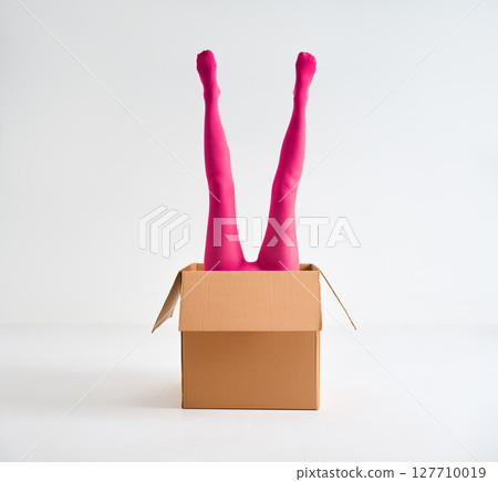 Female legs in bright pink tights raised up from open cardboard box Female legs in bright pink tights raised up from open cardboard box 127710019