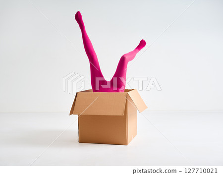 Female legs in bright pink tights sticking out of open cardboard box Female legs in bright pink tights sticking out of open cardboard box 127710021