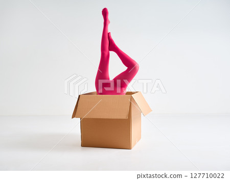 Female legs in bright pink tights raised up from open cardboard box Female legs in bright pink tights raised up from open cardboard box 127710022