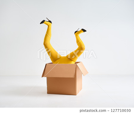 Female legs in yellow tights and high heels shoes raised up in open cardboard box Female legs in yellow tights and high heels shoes raised up in open cardboard box 127710030
