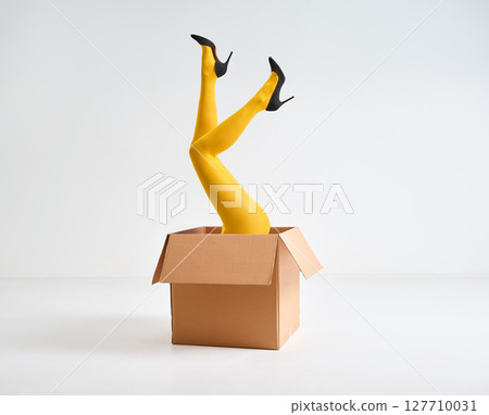 Female legs in yellow tights and high heels shoes raised up in open cardboard box Female legs in yellow tights and high heels shoes raised up in open cardboard box 127710031