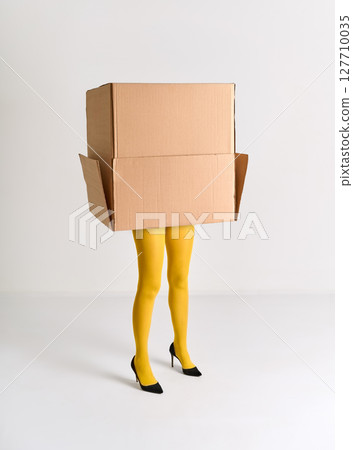 Woman in yellow tights and black high heels hidden under oversized cardboard box 127710035