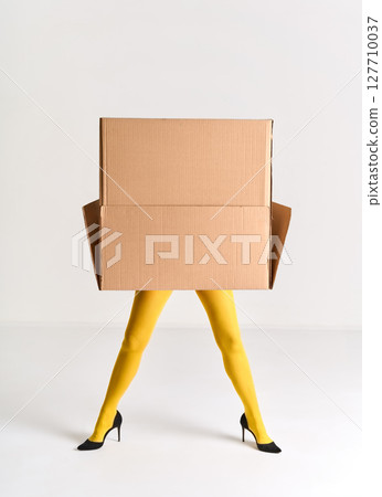 Woman in yellow tights and black high heels hidden under oversized cardboard box Woman in yellow tights and black high heels hidden under oversized cardboard box 127710037
