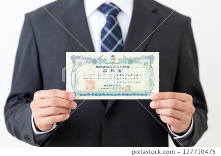 Middle-aged male businessman in a suit holding a stock certificate Middle-aged male businessman in a suit holding a stock certificate 127710475