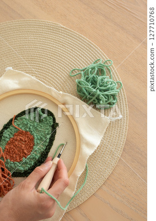 Punch needle embroidery of avocado on hoop with yarn and woman hand. Trendy modern craft hobby 127710768