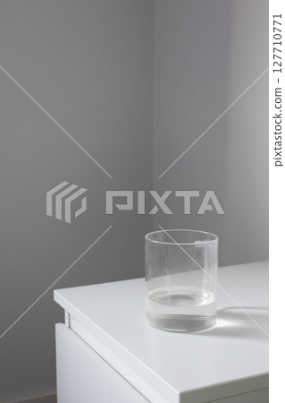 Minimalist glass of water on white bedside table. Health daily routine habits 127710771