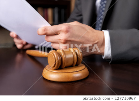 a lawyer works with documents and a wooden gavel in a courtroom or law enforcement office 127710967