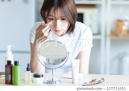 Woman checking her skin in the mirror 127711051