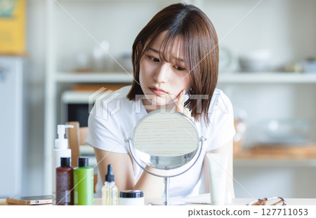 Woman checking her skin in the mirror 127711053