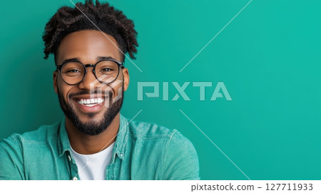 Smiling young man with glasses poses confidently against a vibrant green background in a studio setting 127711933