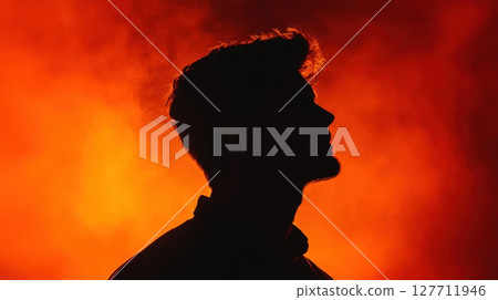 Silhouetted figure against a vivid orange background, capturing a moment of contemplation during an atmospheric event in the evening dusk 127711946