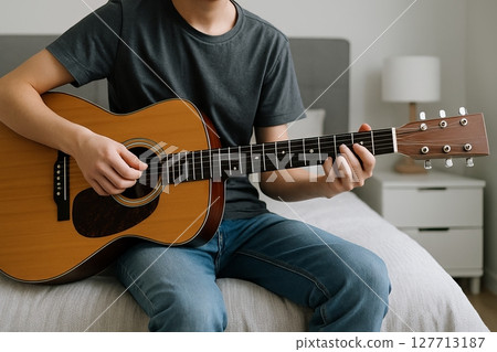 Young man playing acoustic guitar in bedroom setting. concept of musical learning, relaxation, creative expression Young man playing acoustic guitar in bedroom setting. concept of musical learning, relaxation, creative expression 127713187
