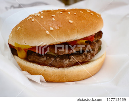 A double meat burger with ketchup and mustard on it, sitting in paper takeout container 127713669