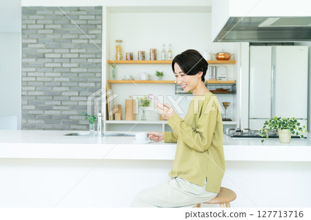 Middle-aged woman using a smartphone in the kitchen Middle-aged woman using a smartphone in the kitchen 127713716