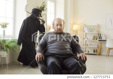 Death in Grim Reaper disguise comes to elderly man who's sitting in armchair at home 127713751