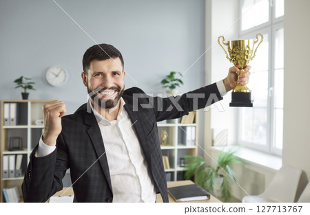 Excited happy man holding the trophy award for success in business standing in office 127713767