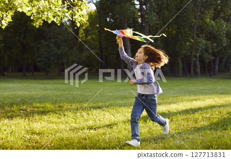 Happy kid running on green field, holding colorful kite and enjoying carefree summer day in nature. Happy kid running on green field, holding colorful kite and enjoying carefree summer day in nature. 127713831