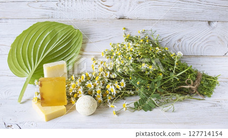 Handmade herbal soap and chamomile flowers on white wooden background. 127714154