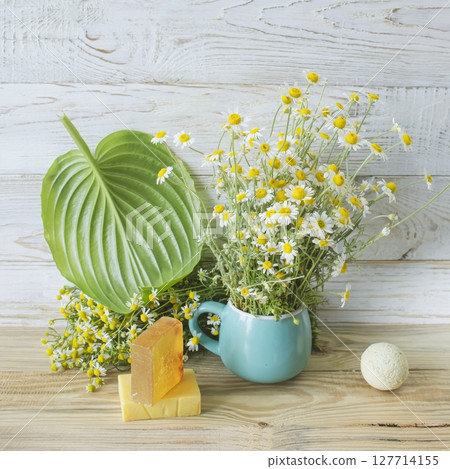 Handmade herbal soap and chamomile flowers on white wooden background. 127714155