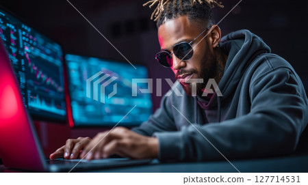 A man with dreadlocks sitting at a desk using a laptop computer 127714531
