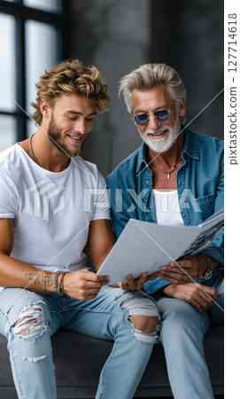 A man and a man sitting on a couch looking at a magazine 127714618