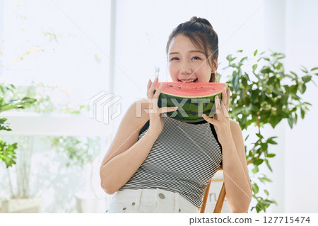 Summer lifestyle of a young woman eating watermelon in her room 127715474