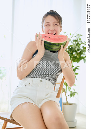 Summer lifestyle of a young woman eating watermelon in her room 127715477