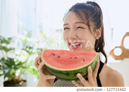 Summer lifestyle of a young woman eating watermelon in her room 127715482