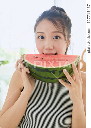 Summer lifestyle of a young woman eating watermelon in her room 127715487