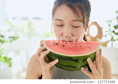 Summer lifestyle of a young woman eating watermelon in her room 127715488