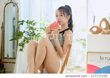Summer lifestyle of a young woman eating watermelon in her room 127715500