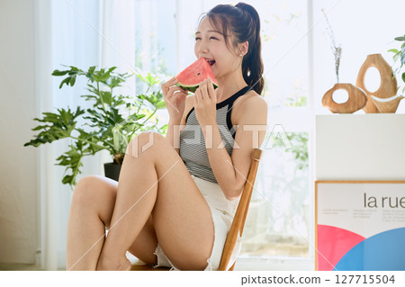 Summer lifestyle of a young woman eating watermelon in her room 127715504