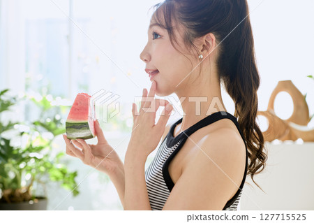 Summer lifestyle of a young woman eating watermelon in her room Summer lifestyle of a young woman eating watermelon in her room 127715525