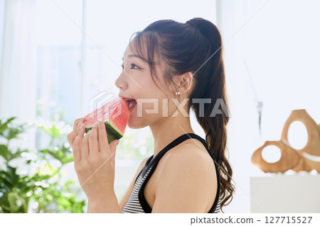 Summer lifestyle of a young woman eating watermelon in her room 127715527