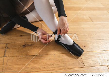 Ballerina puts on pointe shoes on leg in dance class. Classical ballet dancer woman in dance studio. Ballerina putting on tying classical pointe shoes for dance training. Ballet school concept Ballerina puts on pointe shoes on leg in dance class. Classical ballet dancer woman in dance studio. Ballerina putting on tying classical pointe shoes for dance training. Ballet school concept 127715819