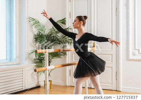 Young ballerina in tutu skirt stretching practicing ballet positions dancing near ballet barre in dance class. Young classical dancer woman in dance studio. Ballet class training Ballet school concept Young ballerina in tutu skirt stretching practicing ballet positions dancing near ballet barre in dance class. Young classical dancer woman in dance studio. Ballet class training Ballet school concept 127715837