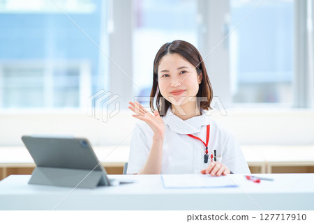 A woman in a white coat sitting at a table 127717910